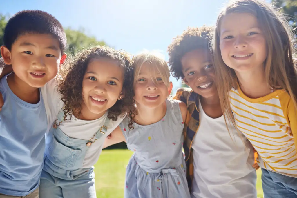 Happy smile and portrait of kids in a park playing together outdoor in nature with friendship Happiness diversity and children friends standing embracing and bonding in a outside green garden - Oxford Athletic Club
