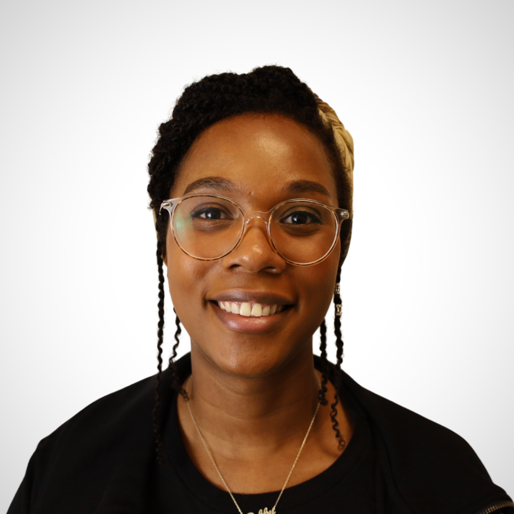 Smiling woman with round glasses and braided hair against a light background.
