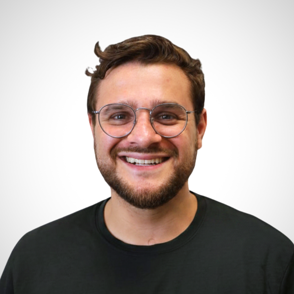 Smiling man with round glasses and a beard wearing a black shirt, against a light gray backdrop.