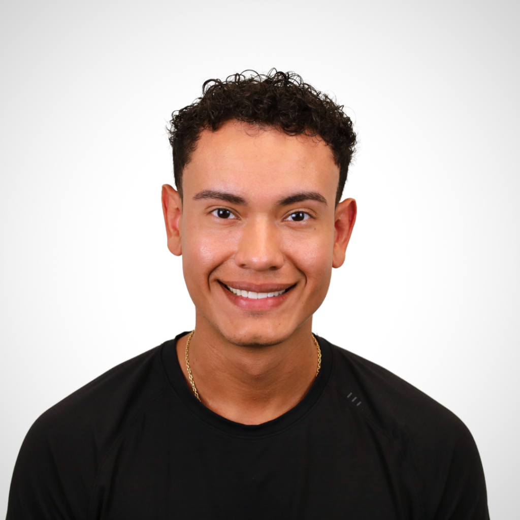 Portrait of a smiling young man with short curly hair wearing a black shirt, against a light gray background.